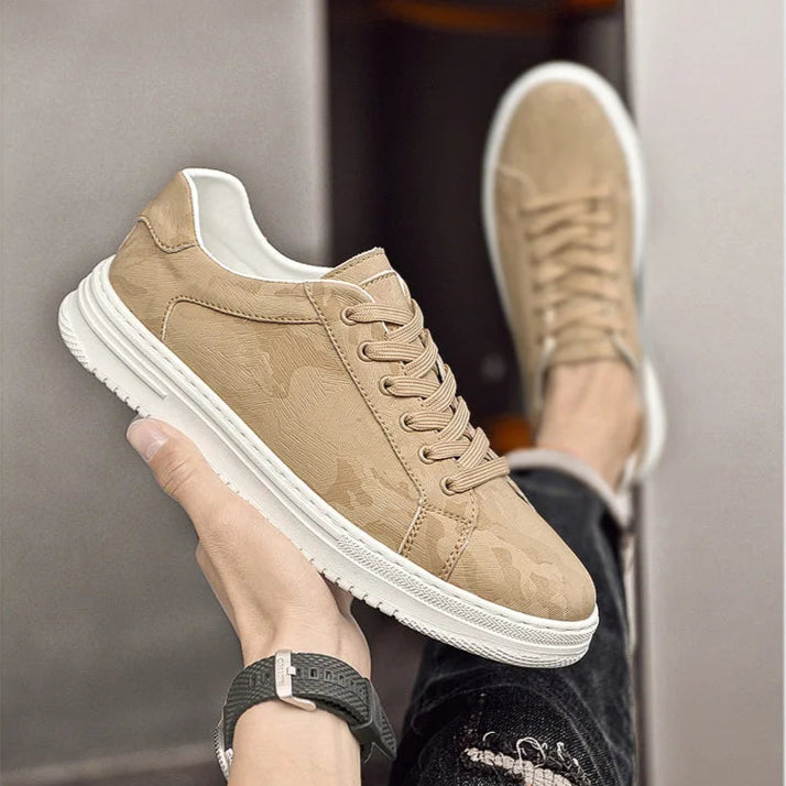 Beige sneaker with white sole held by a hand against a neutral background