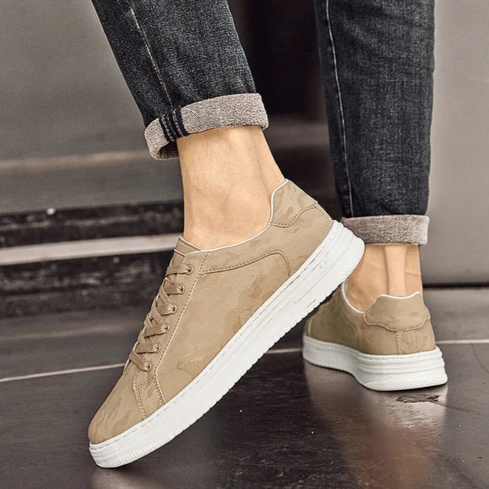 Beige sneakers with white soles worn with dark jeans on a neutral background