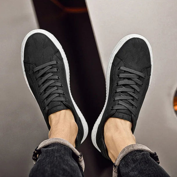 Black sneakers with white soles worn by a person sitting on a chair.