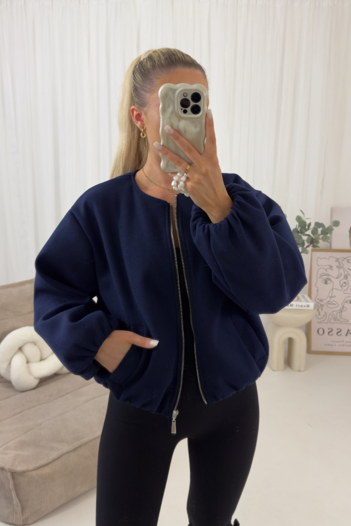 Person wearing a navy blue sweatshirt taking a mirror selfie in a room with a couch and decorative items.