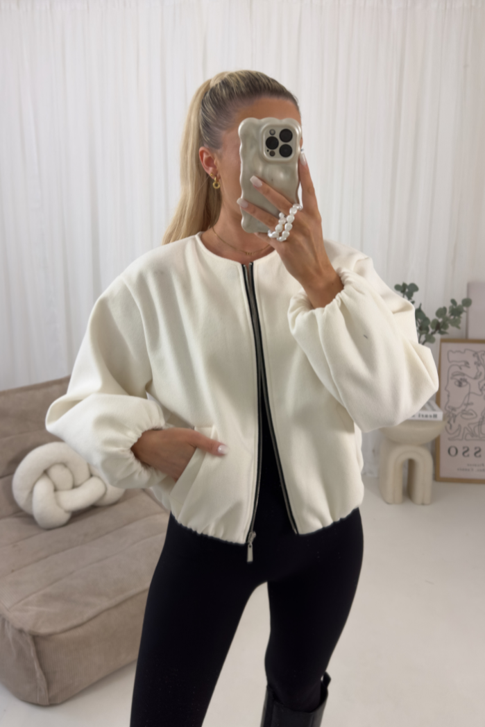 Person wearing a white bomber jacket in a minimalistic room.