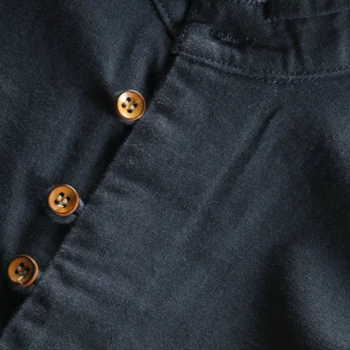 Close-up of a dark blue shirt with gold buttons and a brand tag on a light gray background.