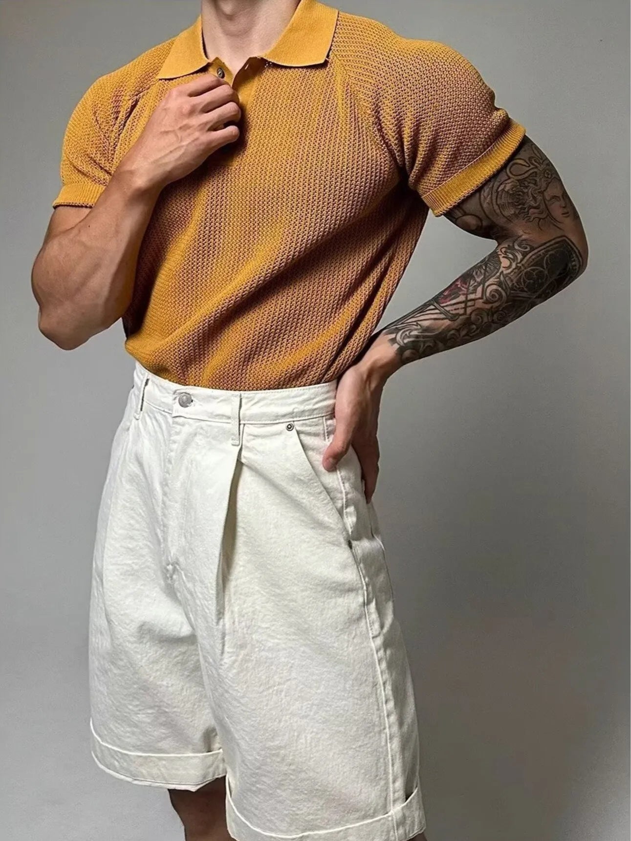 Person wearing a mustard yellow textured polo shirt and white shorts on a gray background