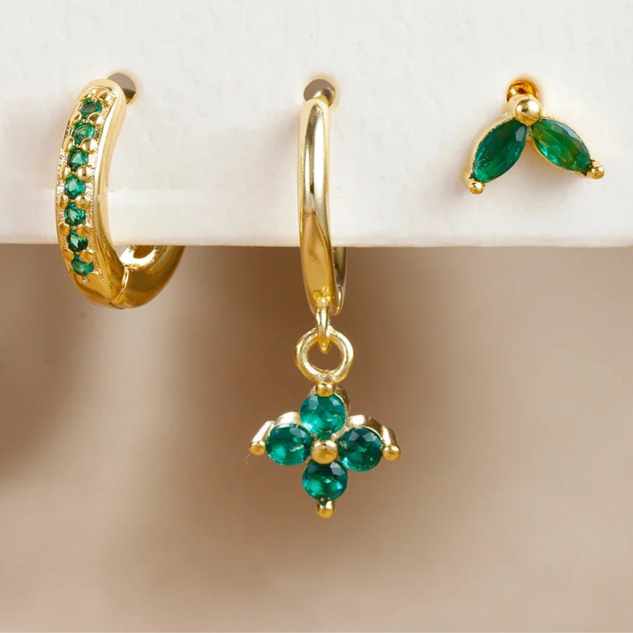 Gold earrings with green gemstones on a white and beige gradient background