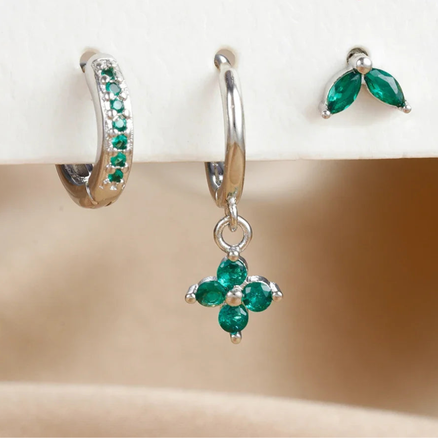 Silver earrings with green gemstones on a beige surface