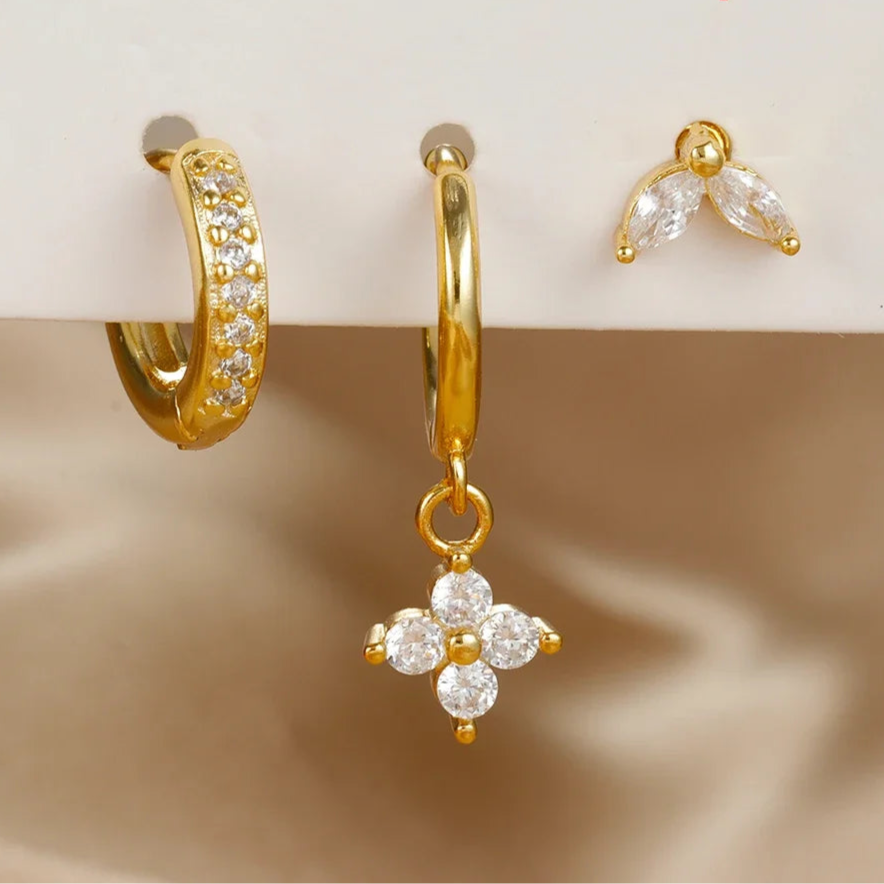 Set of gold earrings with clear stones on a beige background