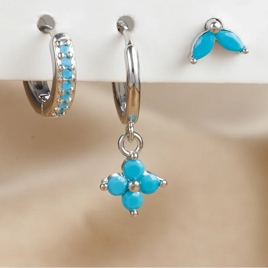 Set of three turquoise flower-shaped earrings on a beige background