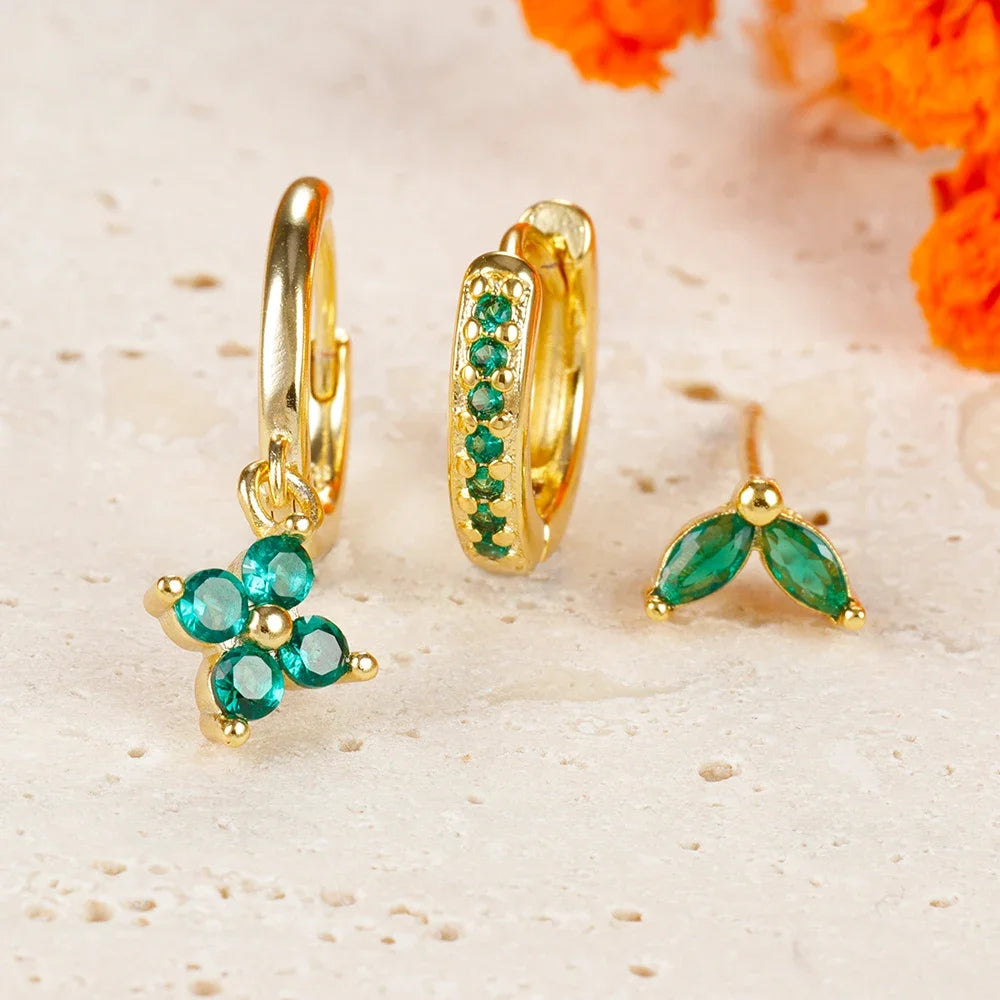 Gold hoop earrings with green gemstones on a textured beige surface with orange flowers.