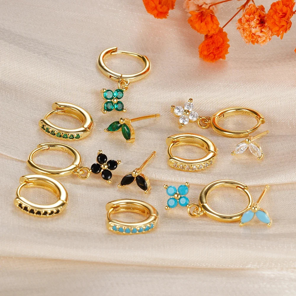 Collection of gold hoop earrings with gemstone accents on a beige surface with orange flowers.