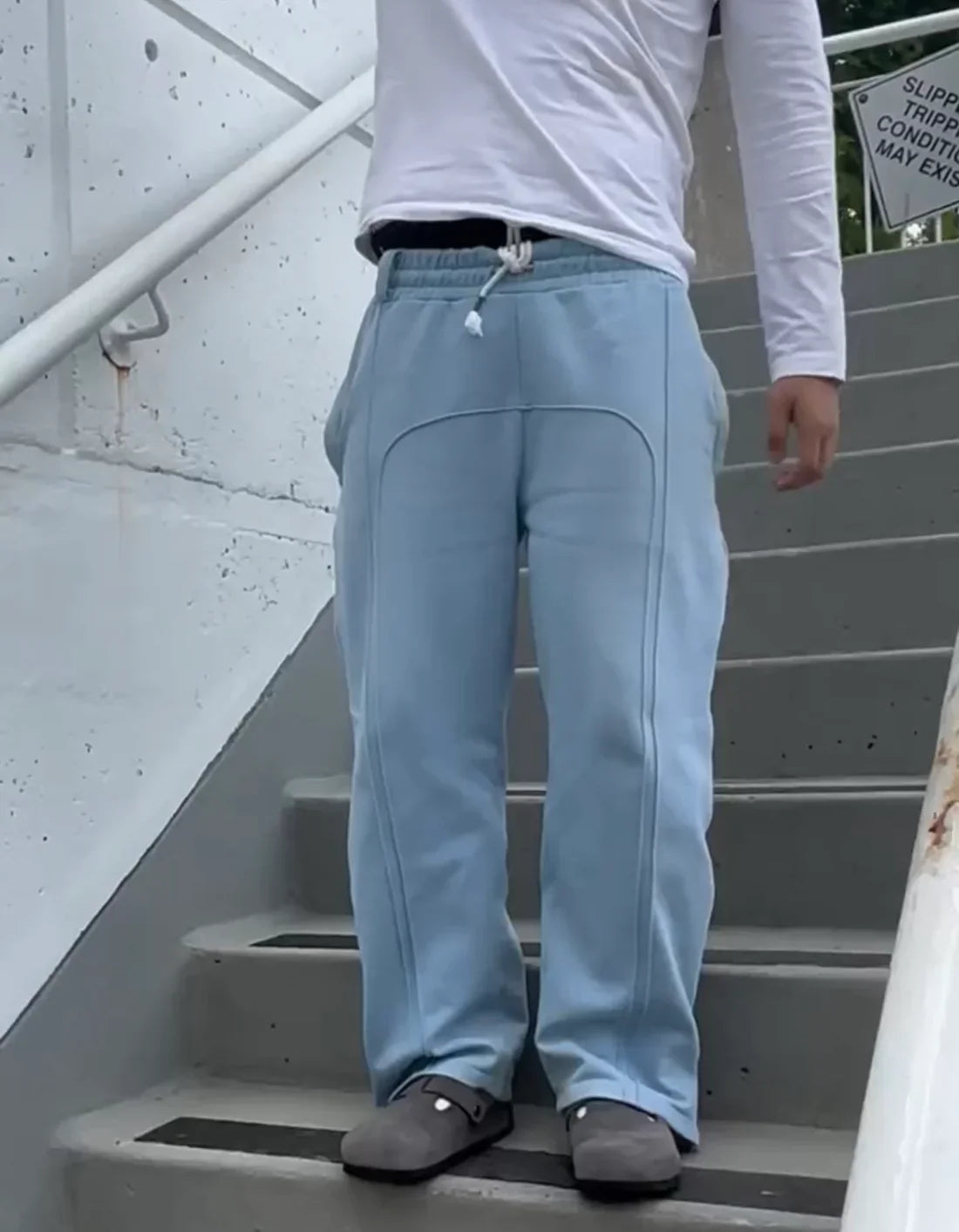 Person wearing light blue pants and a white long-sleeve shirt on a staircase.