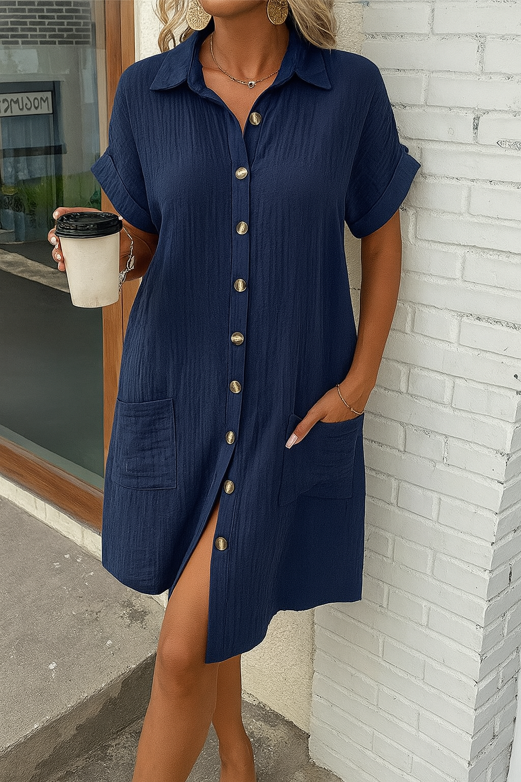 Woman wearing a navy blue button-up dress against a white brick wall.