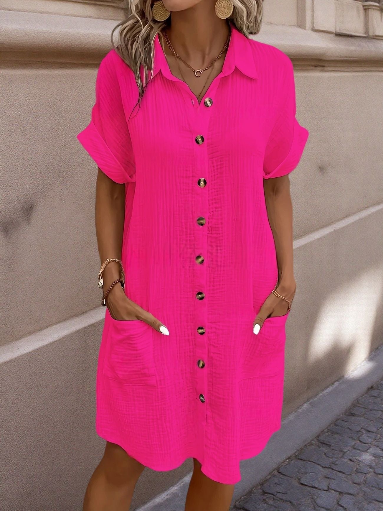 Woman wearing a bright pink dress with black buttons against a beige wall.