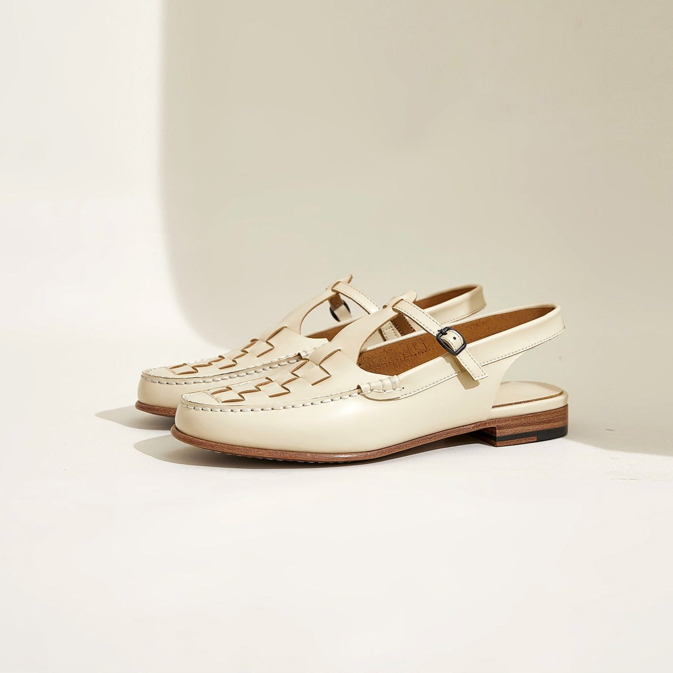 Pair of cream-colored loafers with brown soles on a light beige background