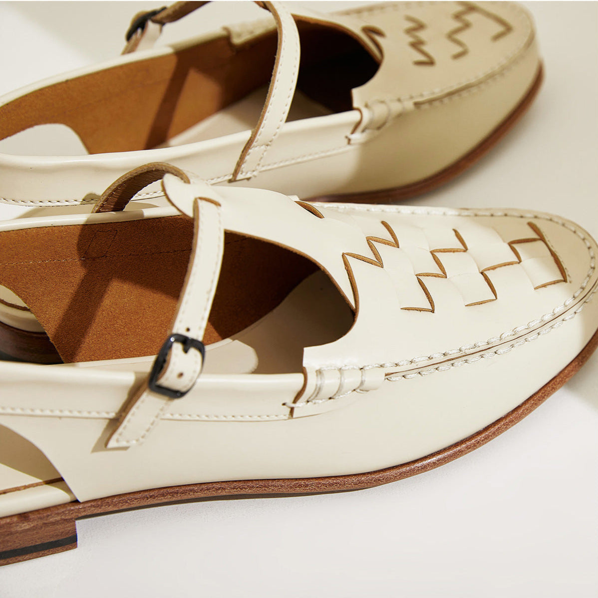 Pair of white sandals with brown soles on a light background