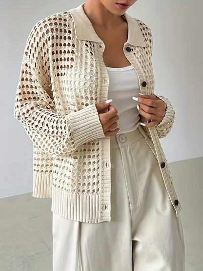 Person wearing a beige knitted cardigan with black buttons on a plain background