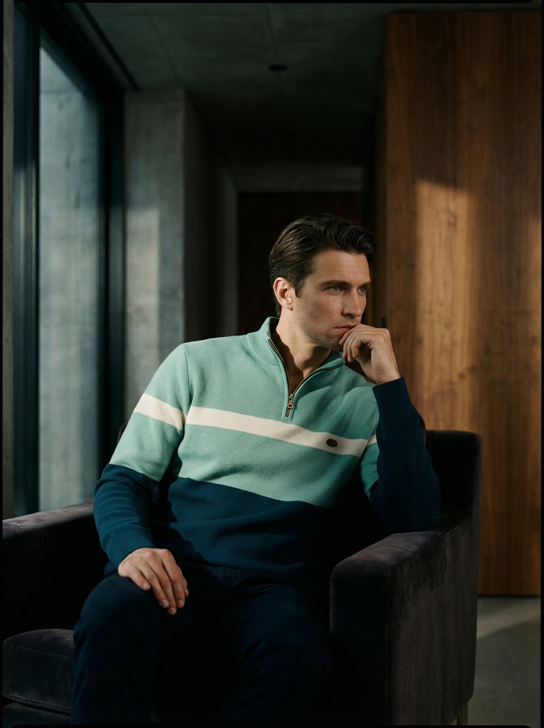 Man sitting in a modern interior setting wearing a light blue and green striped sweater.
