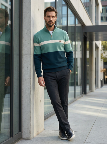 Man wearing a green and navy sweater with a white stripe, standing against a modern building.
