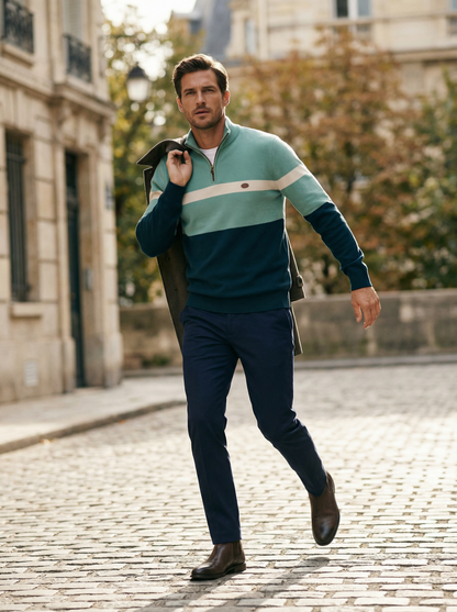 Man walking on a street wearing a striped sweater and dark pants.