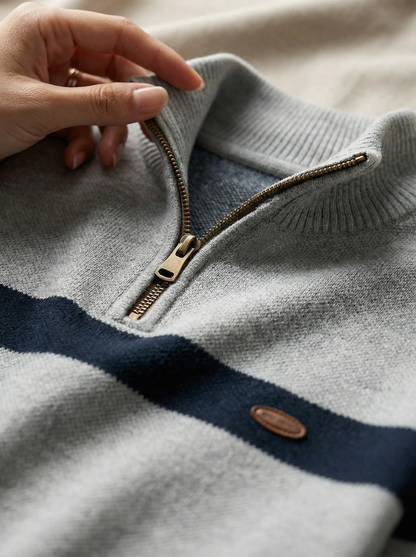 Close-up of a gray sweater with a zipper and button, held by a hand.