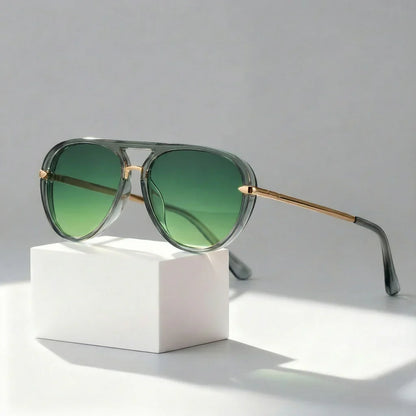 Sunglasses with green lenses and gold frames on a white block against a gray background