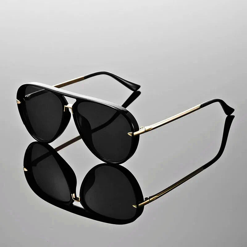 Black sunglasses with gold frames on a reflective gray surface