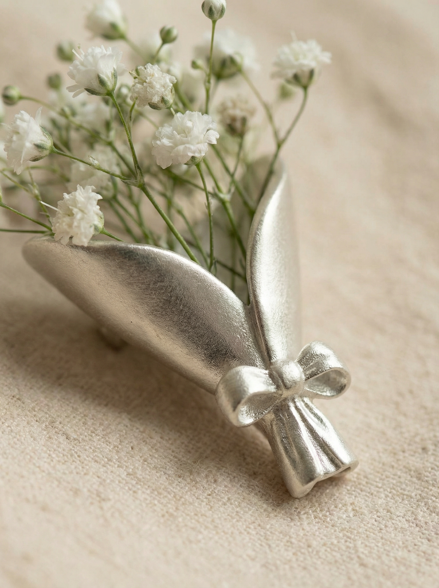 Silver decorative vase with a bow holding small white flowers on a beige surface