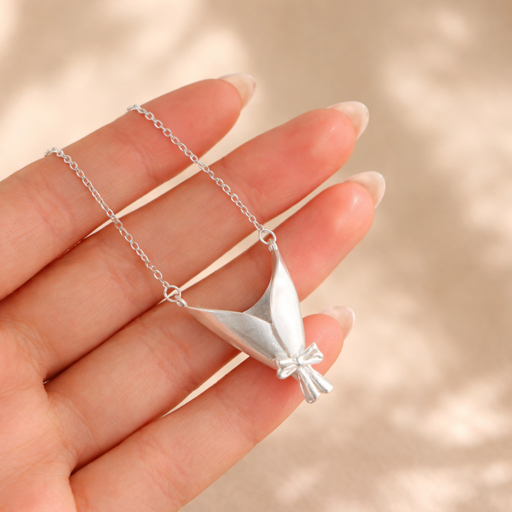 Silver necklace with a leaf-shaped pendant held by a hand against a beige background