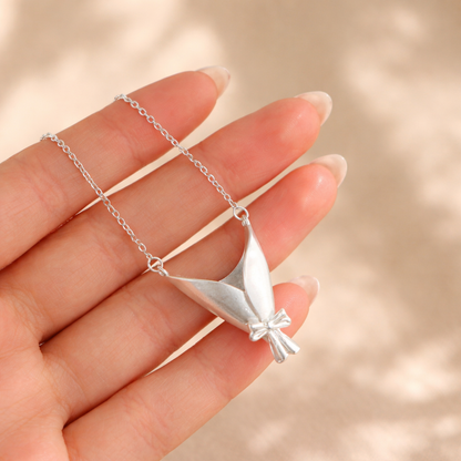 Silver necklace with a leaf-shaped pendant held by a hand against a beige background