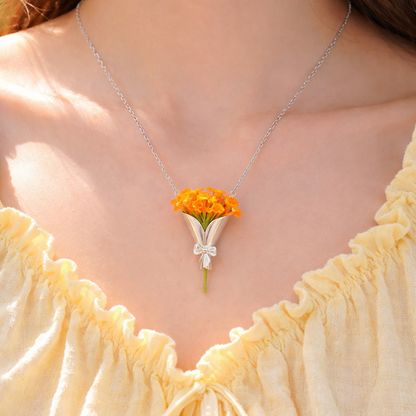 Necklace with a pendant shaped like a bouquet of orange flowers worn by a person in a yellow top.