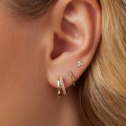 Close-up of an ear wearing gold hoop earrings with small diamond studs.