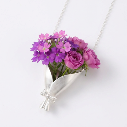 Necklace with a silver vase pendant holding pink and purple flowers on a white background