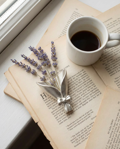 Open book with a cup of coffee and lavender sprigs on a light surface.