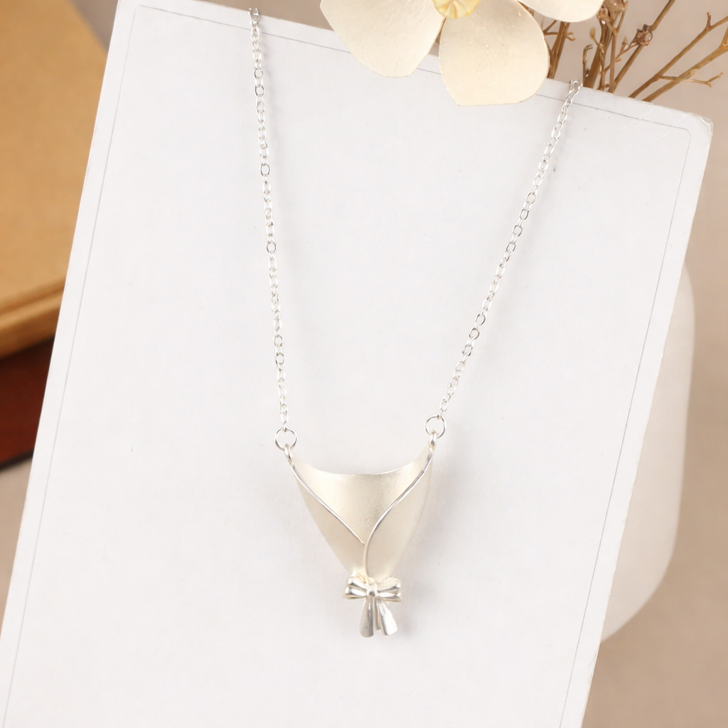 Silver necklace with a pendant on a white stand with a beige background