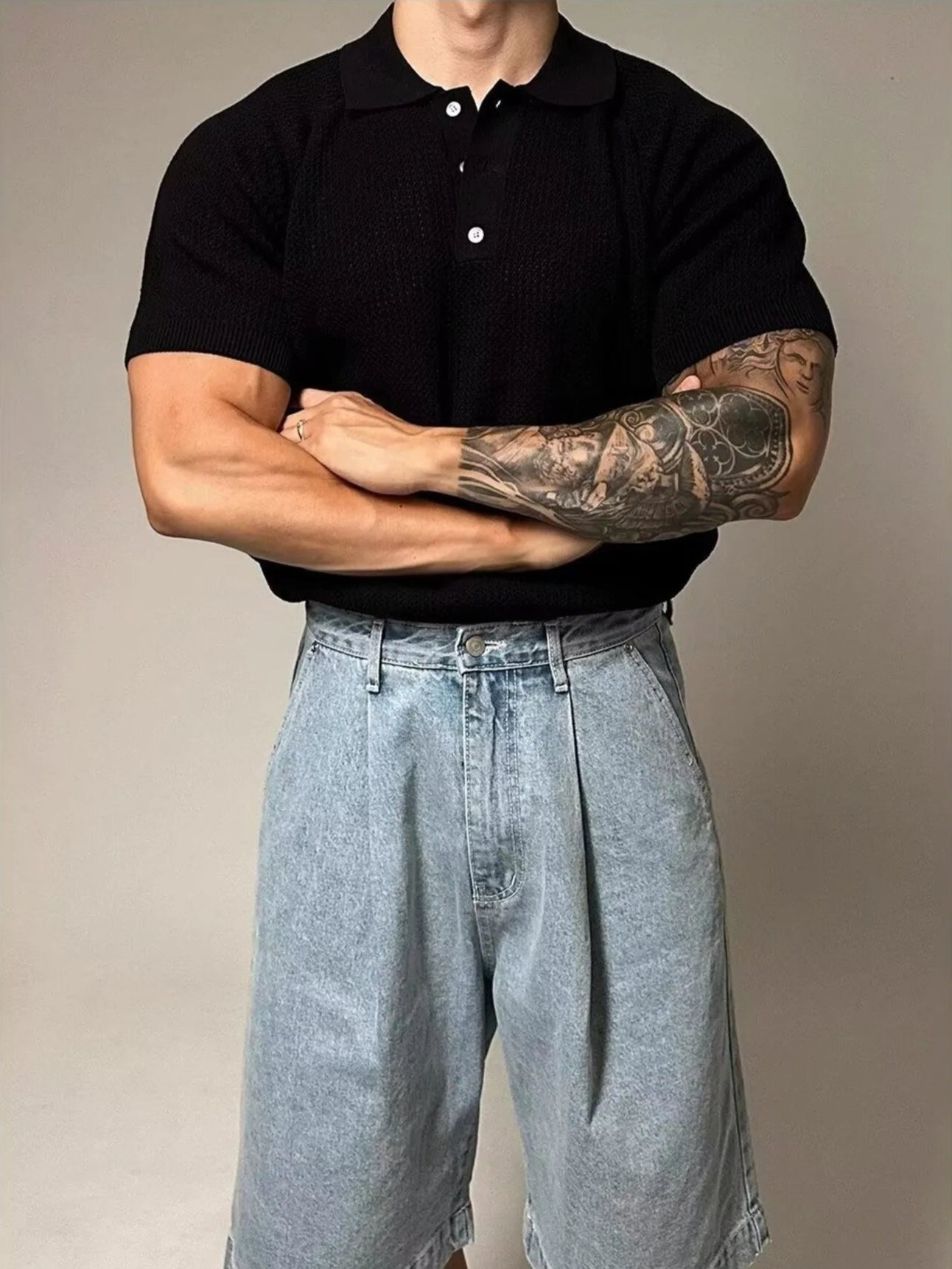 Person wearing a black polo shirt and light blue denim shorts with tattoos on arms.