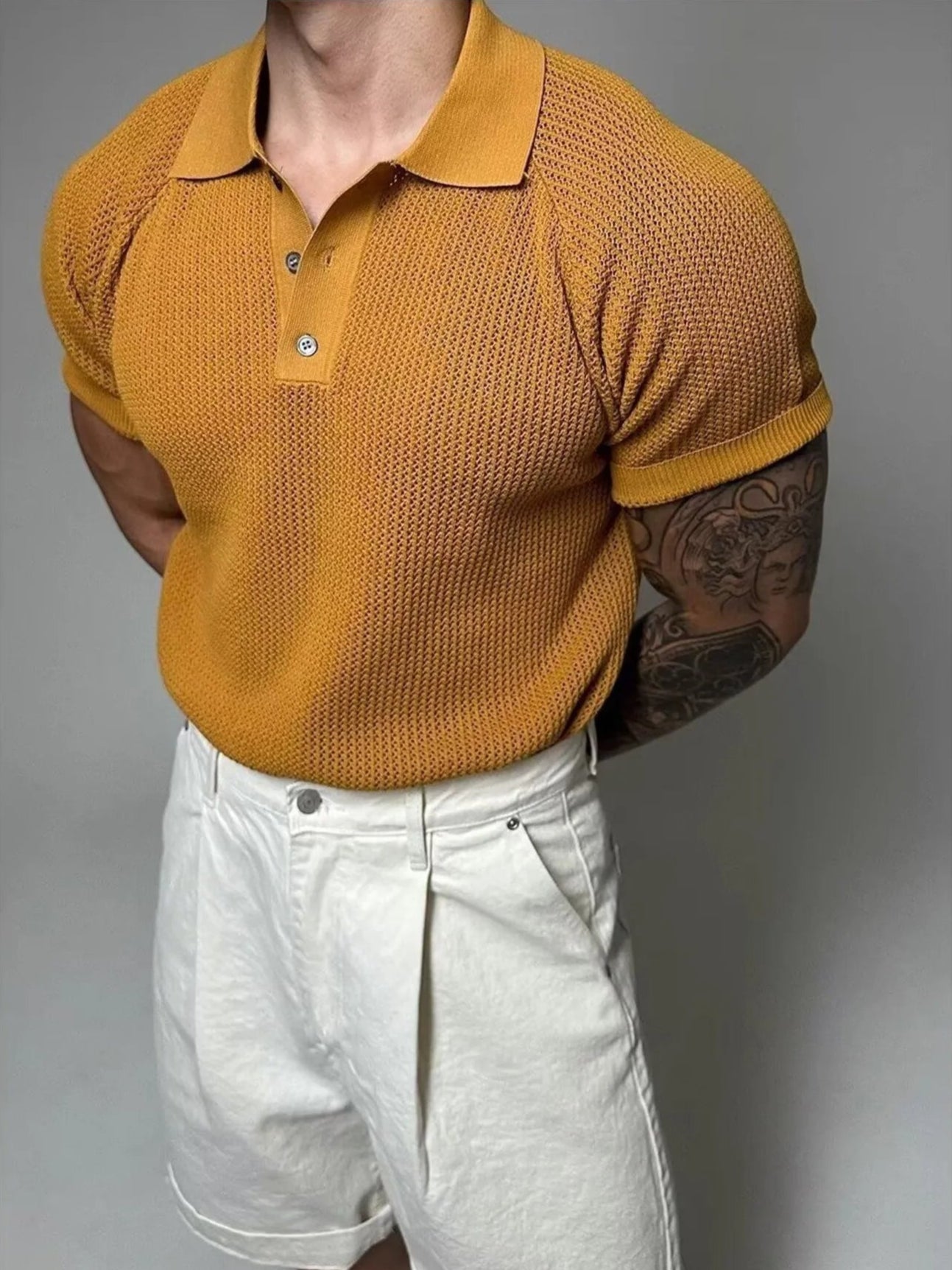 Person wearing a mustard yellow textured polo shirt and light gray shorts against a gray background