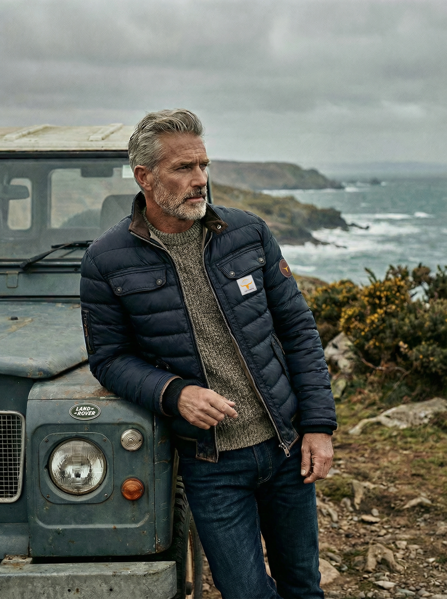 Man standing next to a vintage Land Rover in a coastal setting