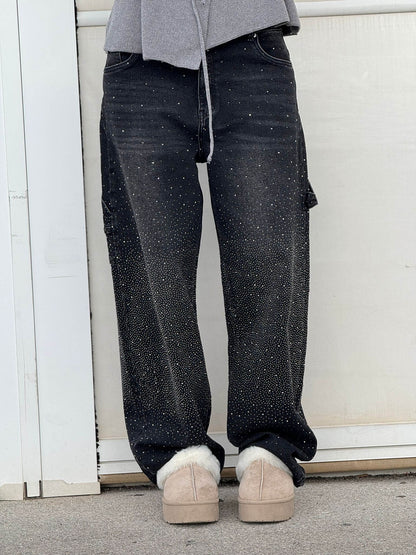 Person wearing black speckled jeans and beige shoes against a white wall.