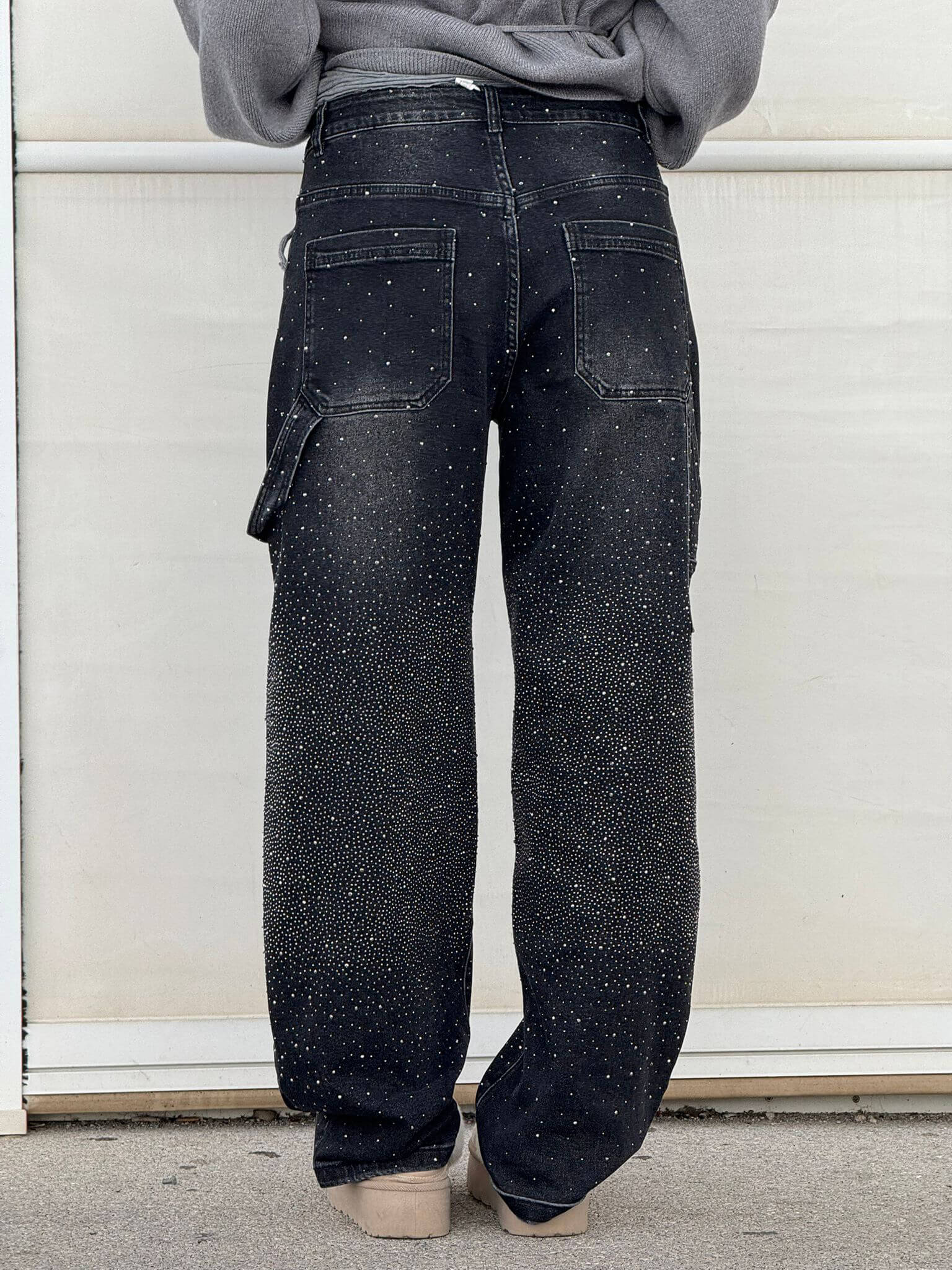 Person wearing black speckled cargo pants against a white wall.