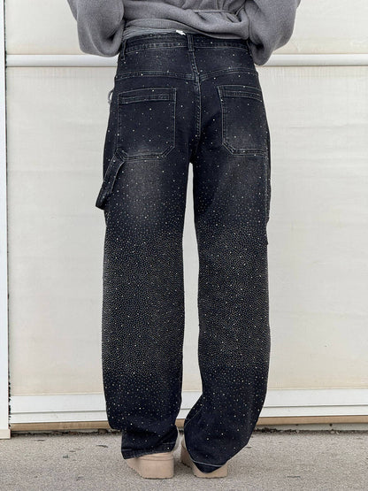 Person wearing black speckled cargo pants against a white wall.