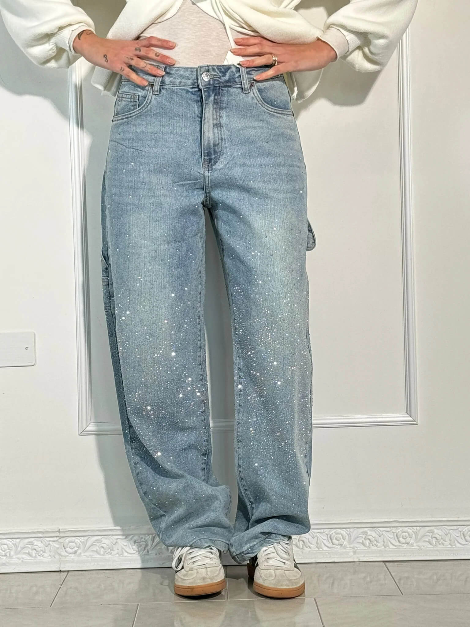 Person wearing light blue jeans and a white sweatshirt against a white wall.