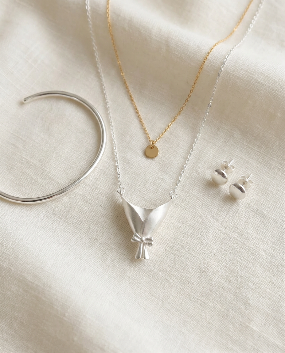 Silver necklace with bow pendant, gold necklace, and silver earrings on a white fabric background