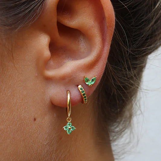 Close-up of an ear wearing gold hoop earrings with green gemstones.