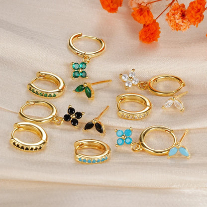 Collection of gold hoop earrings with gemstone accents on a beige surface with orange flowers.