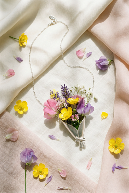 Silver necklace with a floral pendant on a light fabric background with scattered flowers.