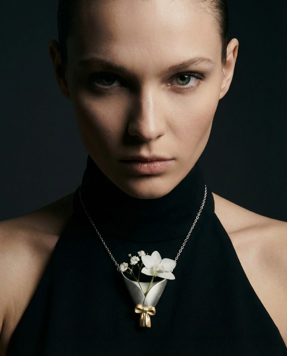 Woman wearing a black turtleneck with a necklace featuring a white flower pendant against a dark background