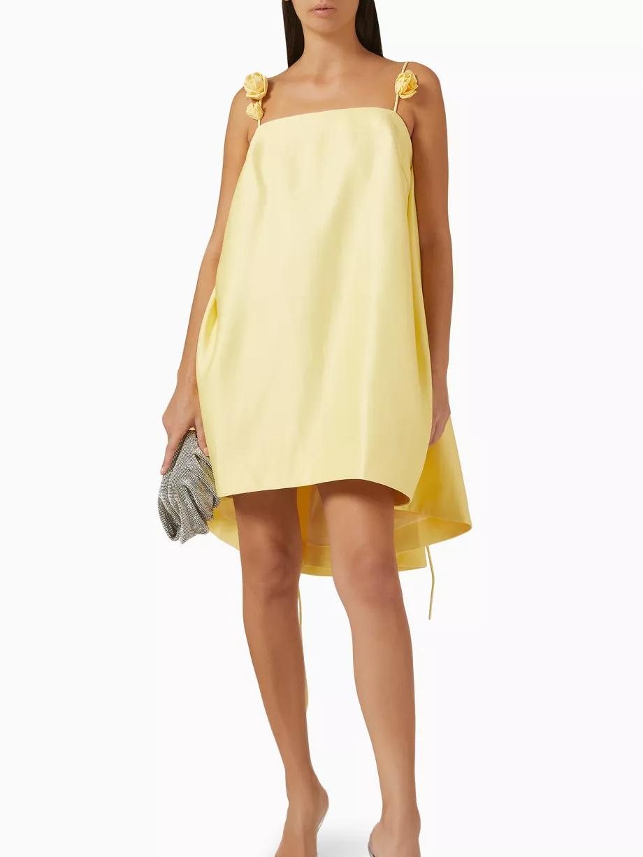 Woman wearing a yellow dress with floral straps on a white background