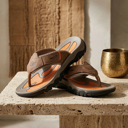 Pair of brown sandals with orange accents on a stone surface.