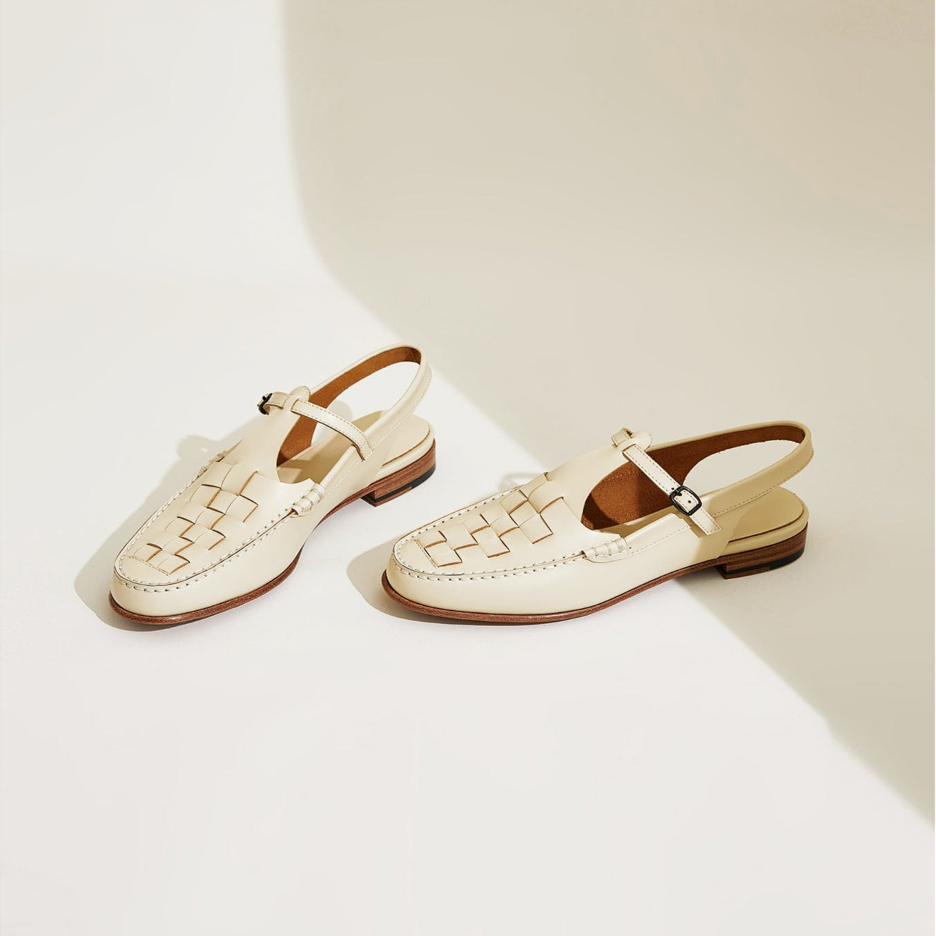 Pair of cream-colored sandals with brown straps on a light background