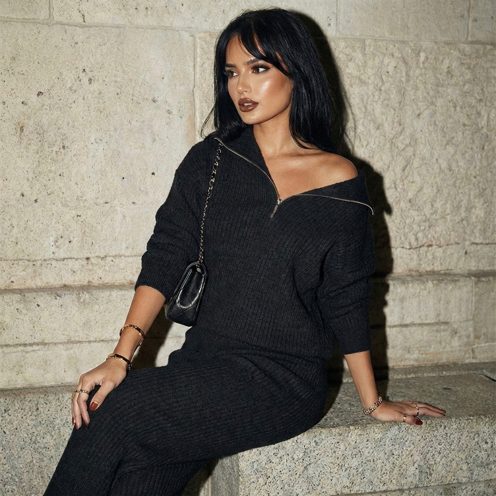 Woman in a black outfit sitting against a stone wall.