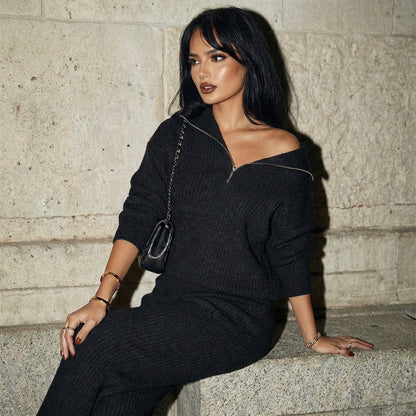 Woman in a black outfit sitting against a stone wall.